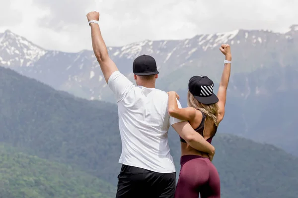 Pareja en traje deportivo abrazando en pico contra las montañas. — Foto de Stock