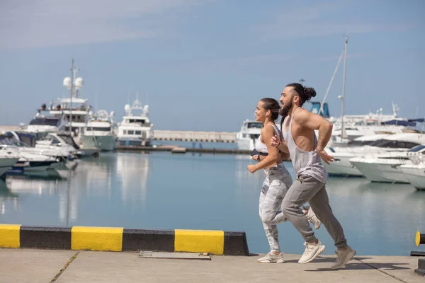 Joven pareja deportiva corriendo sobre el muelle de madera al atardecer — Foto de Stock