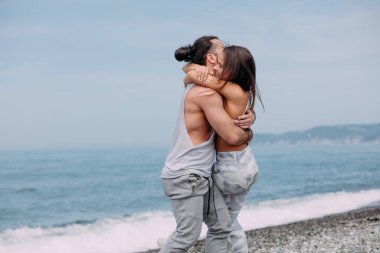 Yaz sabahı kumsalda sarılan bir çift ve arka planda deniz kölesi.