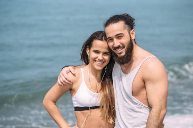 Yaz sabahı kumsalda sarılan bir çift ve arka planda deniz kölesi.