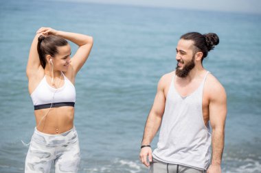 Sportif çift ısınıyor, kumsalda birlikte bacaklarını esnetiyorlar.