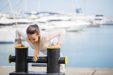 Açık havada antrenman yapan sportif bir kadın okyanus rıhtımında yaya geçidi egzersizi yapıyor..