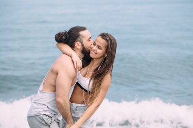 Yaz sabahı kumsalda sarılan bir çift ve arka planda deniz kölesi.