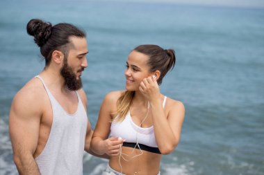 Sportif çift ısınıyor, kumsalda birlikte bacaklarını esnetiyorlar.