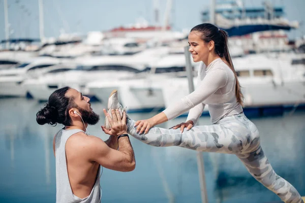 Male coach helping young woman exercising on pier. — Stock Photo, Image
