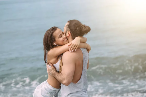 Couple cuddling on beach in summer morning with the sea serf on background — Stock Photo, Image