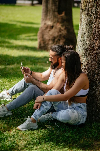 Homem e mulher relaxando com tablet digital no parque após treinamento esportivo — Fotografia de Stock