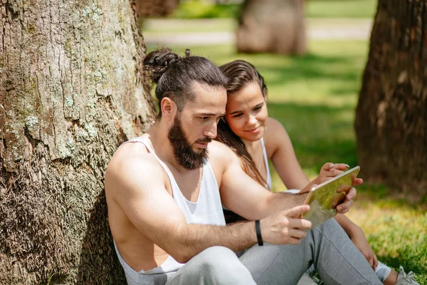 Homme et femme se détendre avec tablette numérique dans le parc après la formation sportive — Photo