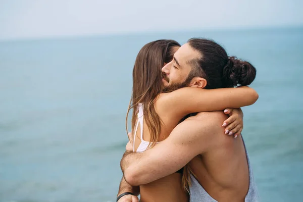 Couple cuddling on beach in summer morning with the sea serf on background — Stock Photo, Image