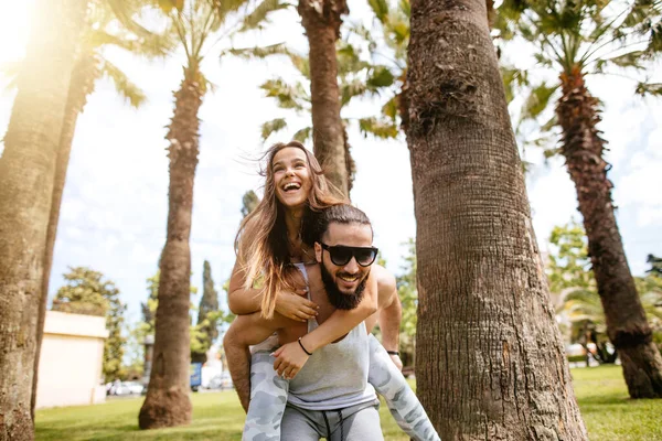 Hommes sportifs ludiques donnant tour de piggyback aux femmes au parc tropical — Photo