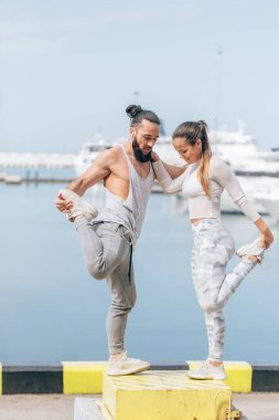 Genç ve güzel bir çift okyanus rıhtımında esneme egzersizleri yapıyor.