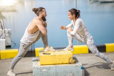 Genç ve güzel bir çift okyanus rıhtımında esneme egzersizleri yapıyor.
