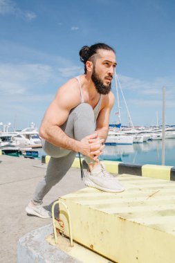 Kumsalda ayakta duran sporcu bacaklarını açıyor.