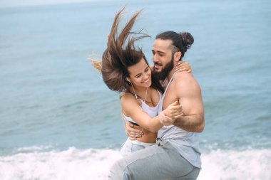 Yaz sabahı kumsalda sarılan bir çift ve arka planda deniz kölesi.