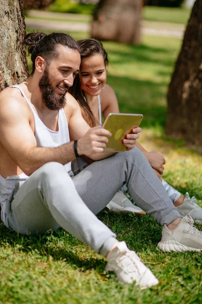 Homme et femme se détendre avec tablette numérique dans le parc après la formation sportive — Photo