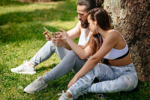 스포츠 훈련을 받은 남자와 여자가 공원에서 디지털 태블릿으로 휴식을 취하는 모습 — 스톡 사진