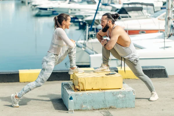 Joven hermosa pareja haciendo ejercicios de estiramiento en el muelle del océano — Foto de Stock