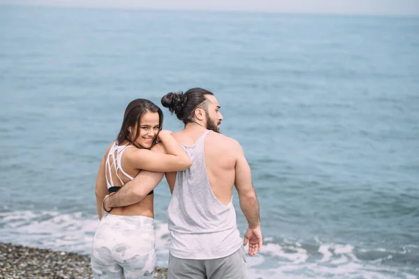 Young fitness couple embracing standing on beach, looking at horizon — Stock Photo, Image