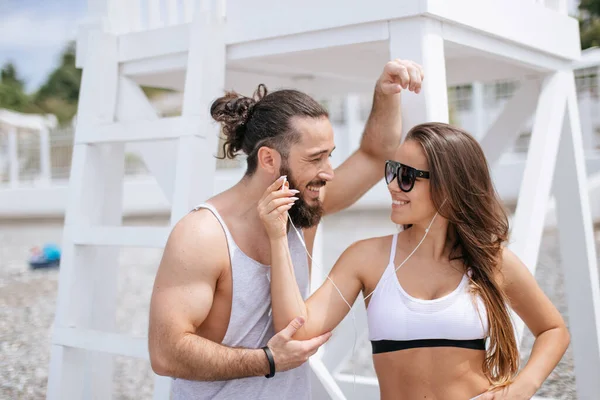 Young couple listening to music using one headphones on beach — Stock Photo, Image