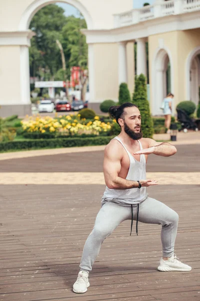 Hombre con barba haciendo sentadillas entrenando al aire libre mostrando poder y fuerza. — Foto de Stock