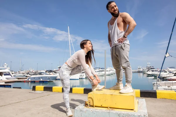 Joven pareja deportiva teniendo un descanso entre el entrenamiento, preparándose para correr en el muelle. — Foto de Stock