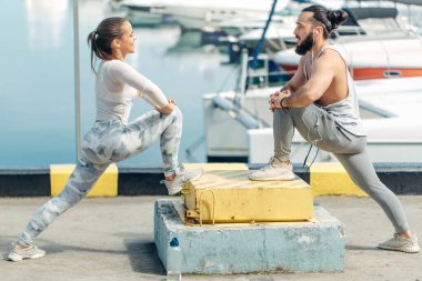 Genç ve güzel bir çift okyanus rıhtımında esneme egzersizleri yapıyor.