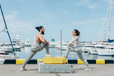Genç ve güzel bir çift okyanus rıhtımında esneme egzersizleri yapıyor.