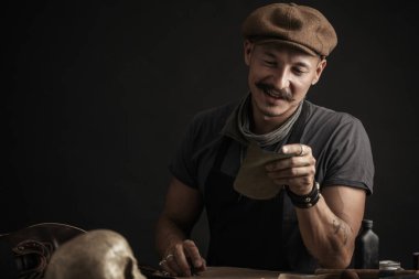 Bıyıklı ayakkabıcı atölyedeki masada ölçüm yapıyor.