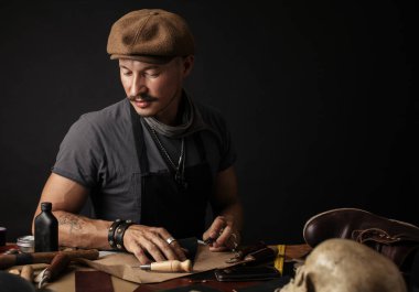 Bıyıklı ayakkabıcı atölyedeki masada ölçüm yapıyor.