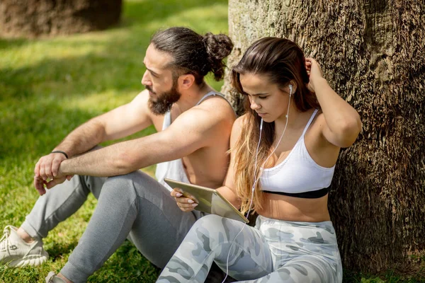 经过体育训练后，公园里的男人和女人都在用数码平板电脑放松一下 — 图库照片