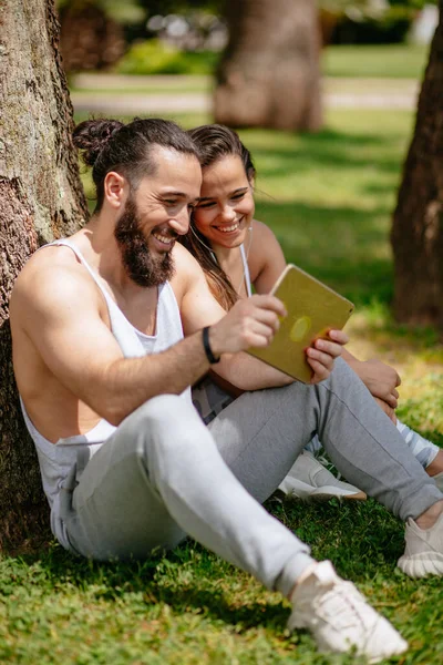 Homme et femme se détendre avec tablette numérique dans le parc après la formation sportive — Photo