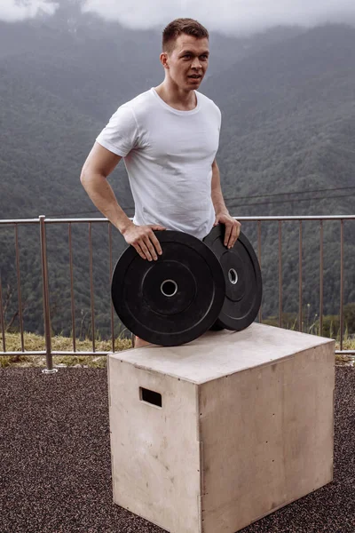 Músculos masculinos fuertes del bombeo del atleta con las placas del peso en entrenamiento al aire libre. — Foto de Stock