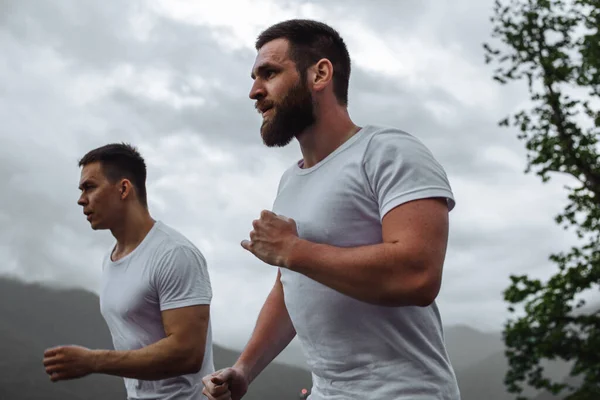 Entrenamiento temprano en la mañana, hombres deportivos corriendo por las montañas viviendo un estilo de vida saludable — Foto de Stock