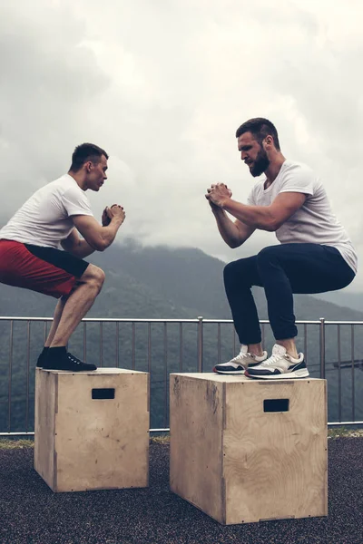 Två manliga atletiska vänner gör box jump motion utomhus — Stockfoto