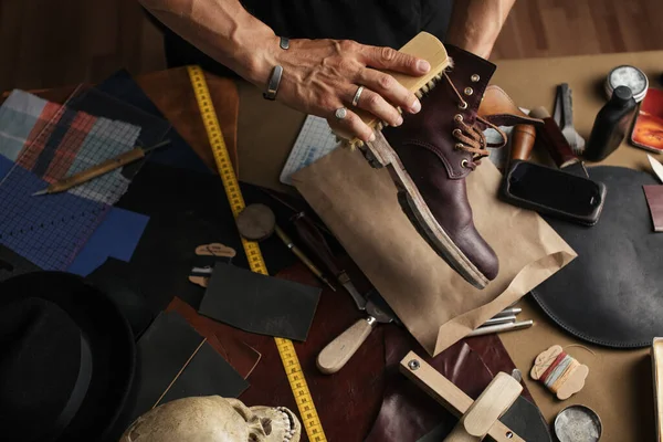 Entretien des chaussures en cuir, gros plan des mains cultivées du cordonnier frottant les bottes — Photo