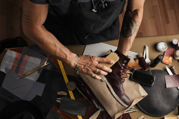 Care for leather shoes, close up of cropped shoemaker hands rubbing up boots