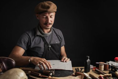 Bıyıklı ayakkabıcı atölyedeki masada ölçüm yapıyor.