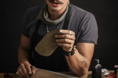 Bıyıklı ayakkabıcı atölyedeki masada ölçüm yapıyor.
