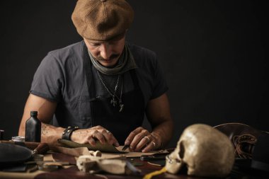 Bıyıklı ayakkabıcı atölyedeki masada ölçüm yapıyor.