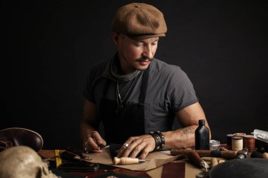 Bıyıklı ayakkabıcı atölyedeki masada ölçüm yapıyor.