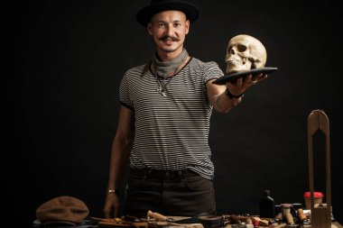 Bıyıklı, şapkalı, kafasında kafatası olan şık bir adam.