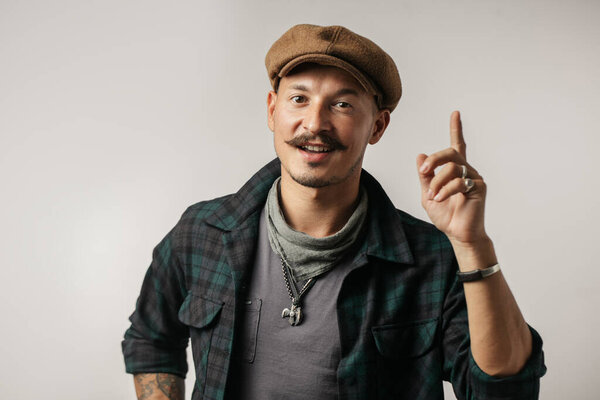 micro-entrepreneur in cap pointing up with his finger isolated on gray