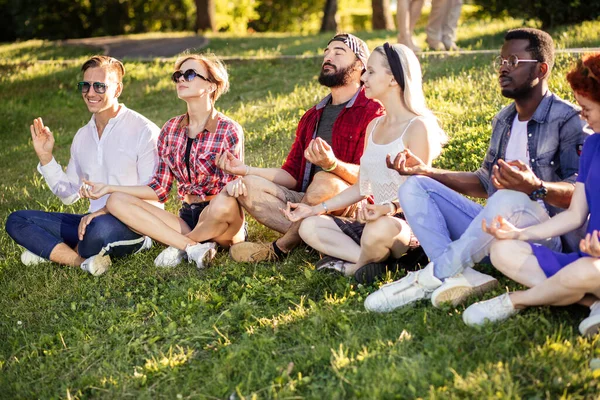 Grupo de amigos adultos meditando mientras practican yoga afuera en el parque. — Foto de Stock