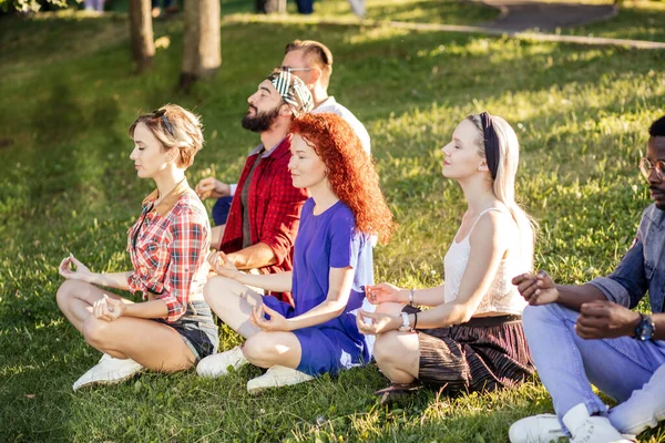 Grupo de amigos adultos meditando mientras practican yoga afuera en el parque. — Foto de Stock