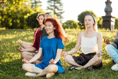 Bir grup yetişkin arkadaş parkta yoga yaparken meditasyon yapıyorlar..