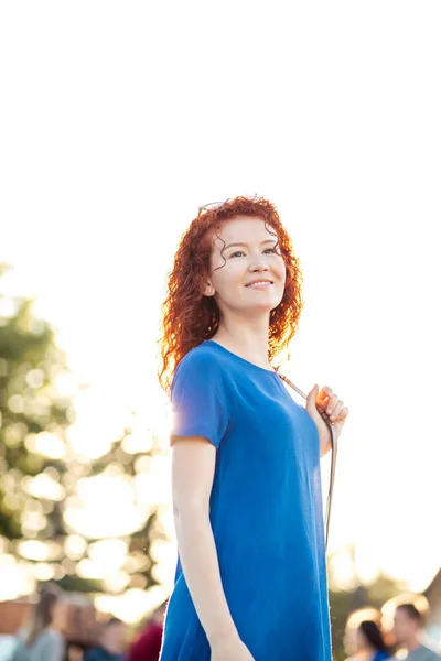 Mujer joven con el pelo rojo rizado ondulado, en vestido azul, en el parque. — Foto de Stock