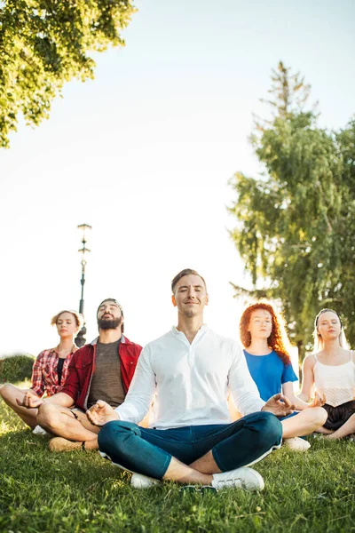 Groupe d'amis adultes méditant tout en pratiquant le yoga à l'extérieur du parc. — Photo