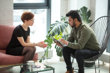 Kadın kanepede oturup Hintli erkek psikologla konuşurken doktor notlar alıyor.