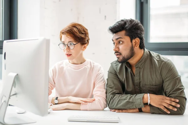 Two surprised coworkers reading news in computer at office