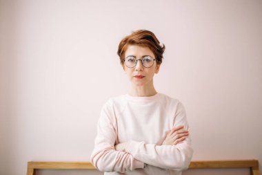 Evde pembe arka planda gözlük takan orta yaşlı bir kadının portresi.